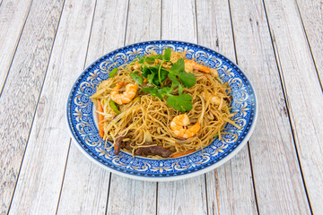 Wok stir-fried Chinese rice noodles with vegetables, shredded beef and peeled prawns on blue plate