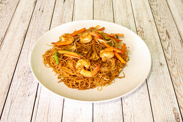 Stir-fried rice noodles with peeled shrimp and vegetables in a wok with recipe from an Asian restaurant