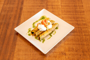 Golden tacos or Mexican flautas with fried corn tortilla stuffed with beans with cream cheese and pico de gallo with green oil and parsley sauce