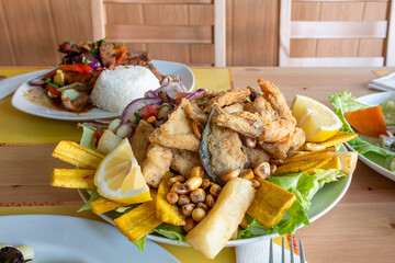 Peruvian recipe for a jalea dish with assorted battered fish, battered prawns and mussels, purple onion, corn of different varieties, fried yucca and fried plantain © Toyakisfoto.photos