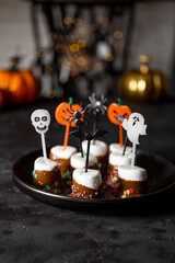 Fototapeta na wymiar Sweet Halloween treat, chocolate covered marshmallows with sugar and Halloween decorations on a black plate, vertical photo with soft focus