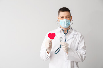 Cardiologist with red heart and stethoscope on light background