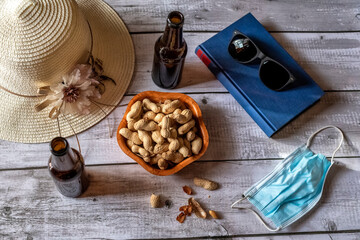 Book, hat, beers and peanuts on a table with a surgical mask.