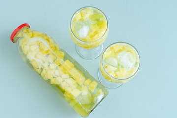 Bottle and two glasses with water and pieces of fruit on blue background. Copy space.