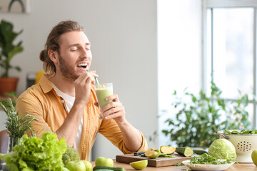 Young man drinking healthy green smoothie in kitchen