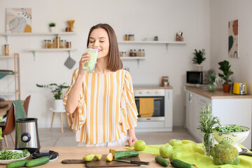 Young woman drinking healthy green smoothie in kitchen