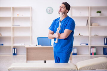 Young male doctor holding human skeleton's hand