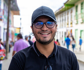 Portrait laughing Latino young man with cap and eyeglasses in a street of a town in Filandia Quindio