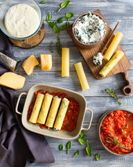 Italian cuisine. Cannelloni with spinach and ricotta. Cannelloni is prepared with parmesan cheese in tomato sauce. Italian dinner. Italian food on a gray wooden background. Bechamel sauce