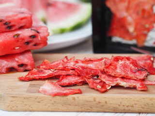 Dried and fresh slices of watermelon on the kitchen board against the grates from the watermelon dryer.