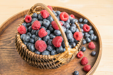 Fresh juicy ripe blueberries and raspberries are in the basket. Garden berries are mixed, closeup