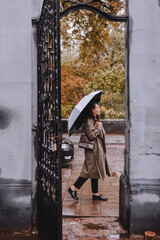 Obraz na płótnie Canvas young pretty woman in autumn outfit walking by city street with umbrella at rainy weather