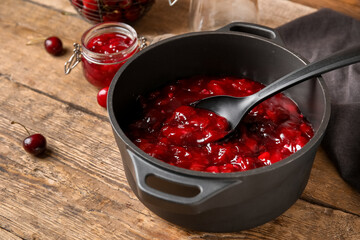 Cooking pot with sweet cherry jam on wooden background