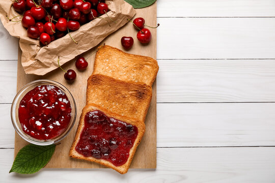 Board with toasts and sweet cherry jam on light wooden background