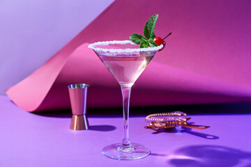 Glass of tasty cosmopolitan cocktail, shaker and strainer on color background