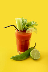 Glass of bloody mary cocktail garnished with cilantro, green chili pepper  and lime on color background