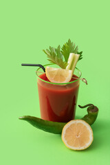 Glass of bloody mary cocktail, green chili pepper and lemon on color background