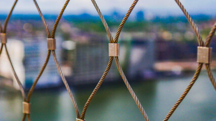Closeup shot of zigzagging steel nets of the fence - river and buildings on background