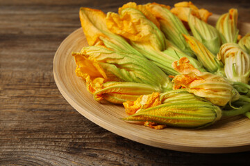 Plate with flowers of zucchini on wooden background, closeup