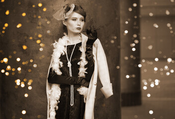 A young beautiful woman in a historical costume of the 20s or 30s of the XX century with a boa and a mouthpiece against the background of lights looks away. High quality photo