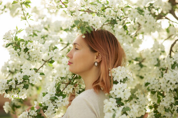 A young woman stands against the background of a blooming apple tree