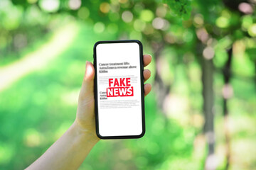 Online fake news on a mobile phone. Holding a smartphone with fake news on vineyard background....