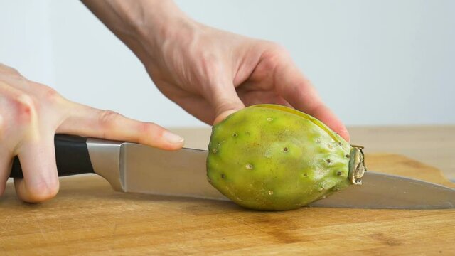 Female hands is cutting a fresh ripe cactus pear or opuntia on a cut wooden board. Exotic fruits, healthy eating concept
