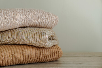 Stack of clean freshly laundered, neatly folded clothes on bedroom dresser's top. Pile of different sweaters of pastel colors in stack. Copy space, close up, background.