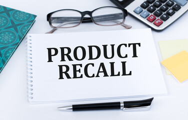 Text Product Recall on a white notepad on a table next to a calculator, glasses and a black pen