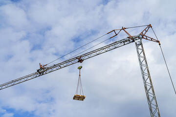 A europallet lifted by a tower crane against a blue sky with light clouds.