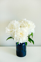 Studio shot of beautiful peony flowers in glass vase on a table over gray wall background with a lot of copy space for text. Feminine floral composition. Close up, backdrop.
