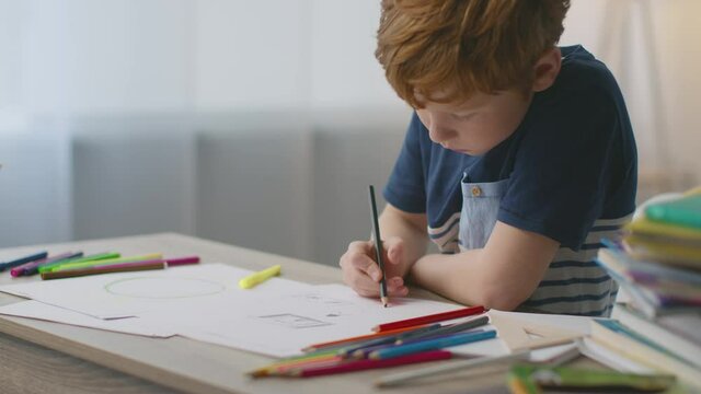 Cute little redhead boy drawing pictures with colorful crayons at home, spending free time alone in room, slow motion