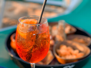 Red glass of aperitif. Appetizers on a green table outdoor. Summer vacation.