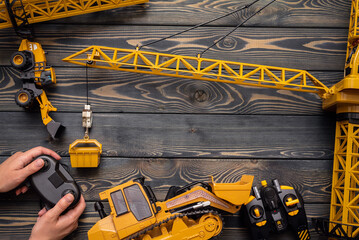 Yellow construction crane toy, bulldozer and hands with a joypad on the wooden flat lay table...