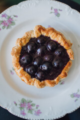high angle view of mini blueberry pie, tart on white porcelain plate with purple flowers