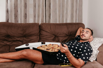 Black man on living room sofa eating pizza and watching streaming.