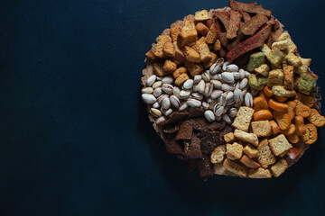 On a wooden stand, snacks from various types of fried breadcrumbs and pistachios are laid out. Dark background, flat lay, copy space.