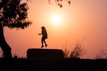 silhouette of a woman jumping with the sun behind, in a warm sunset.