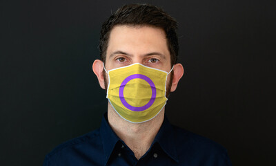 Portrait of an adult man wearing a LGBT intersex flag colors facial mask. LGBT gay rights concept with black background. These colors symbolize the intersex flag.