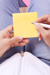 woman writing message on yellow note paper.