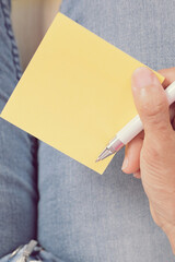 woman writing message on yellow note paper.