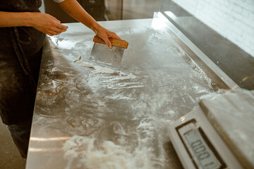 Woman worker cleans metal table from flour in modern craft bakery workshop