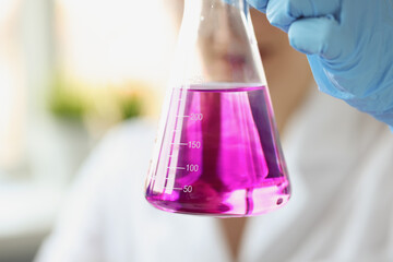 Researcher holds flask of purple liquid with gloves