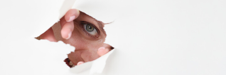 Woman eye looks through hole in white paper