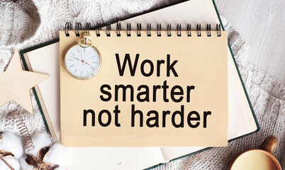 A notebook with the words WORK SMARTER NOT HARDER on a light table, along with a branch of cotton and a clock. Natural light. Festive concept. Top view, flat lay. Spring theme.