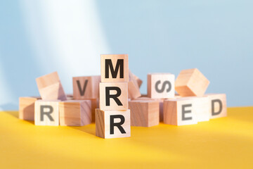 wooden cubes with letters MRR arranged in a vertical pyramid, yellow background