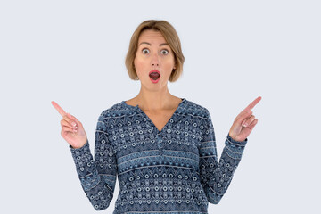 Wow! Very surprised woman points her fingers in different directions. Studio photo on a gray...
