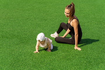 mom and child walk on the green lawn, child learns to crawl