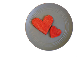 two large red slices of watermelon in the shape of a heart lie side by side on a gray plate on a white background . top view. two hearts