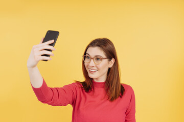 Young woman in eyeglasses standing taking a selfie